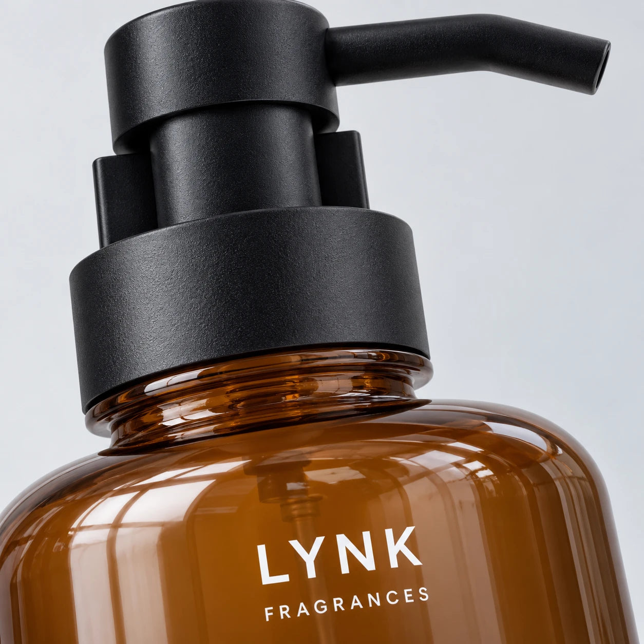 An extreme close-up of the black pump, amber glass and LYNK mark on the White Tea hand-wash bottle.