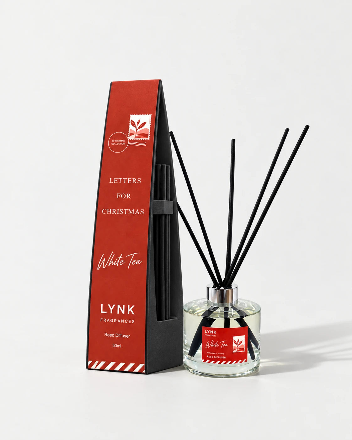 White Tea reed diffuser, black reeds and its red Christmas carton on a pale studio ground.